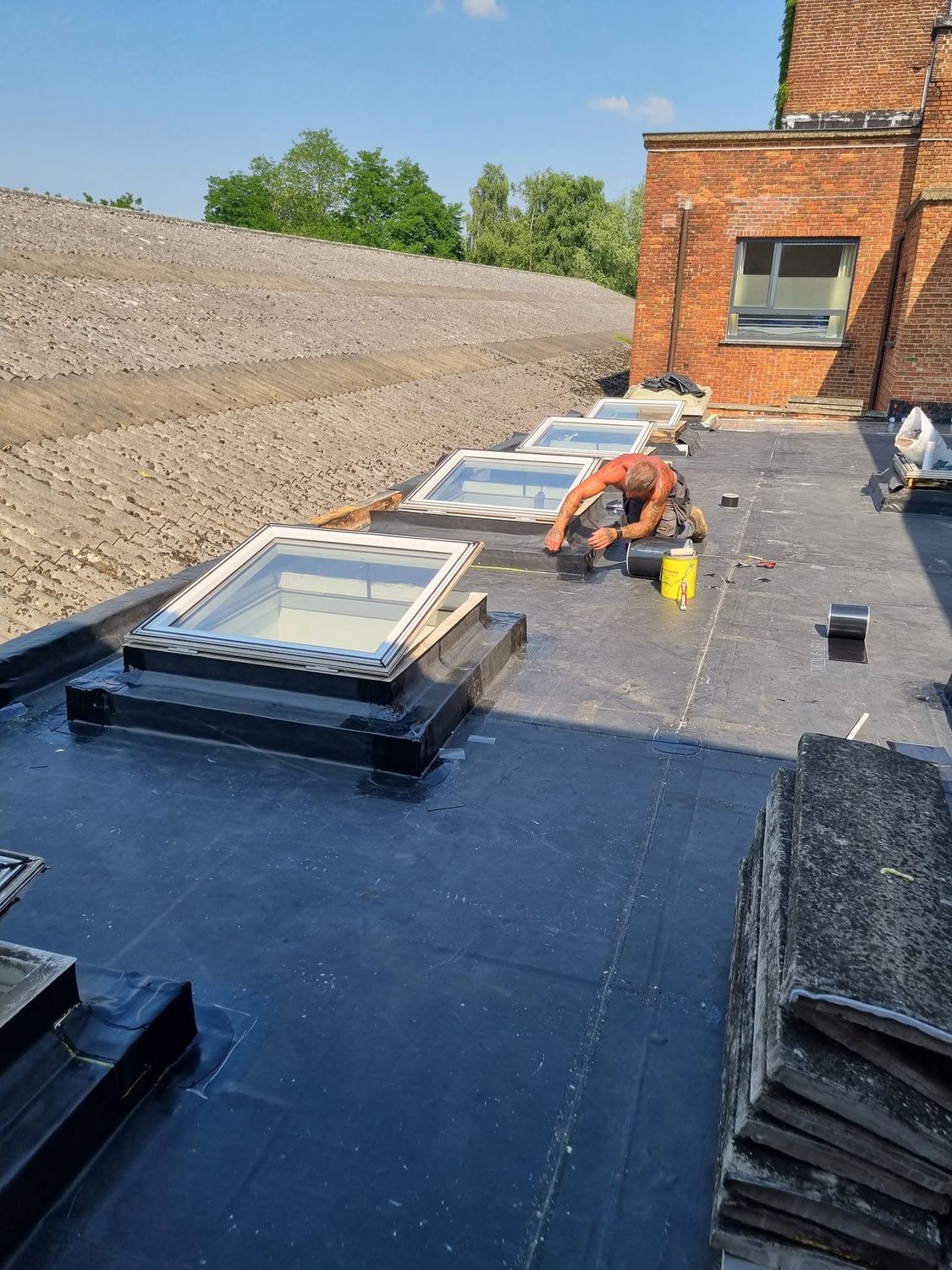 Dakwerker werkt de EPDM waterdicht af rond nieuwe dakvensters op een plat dak
