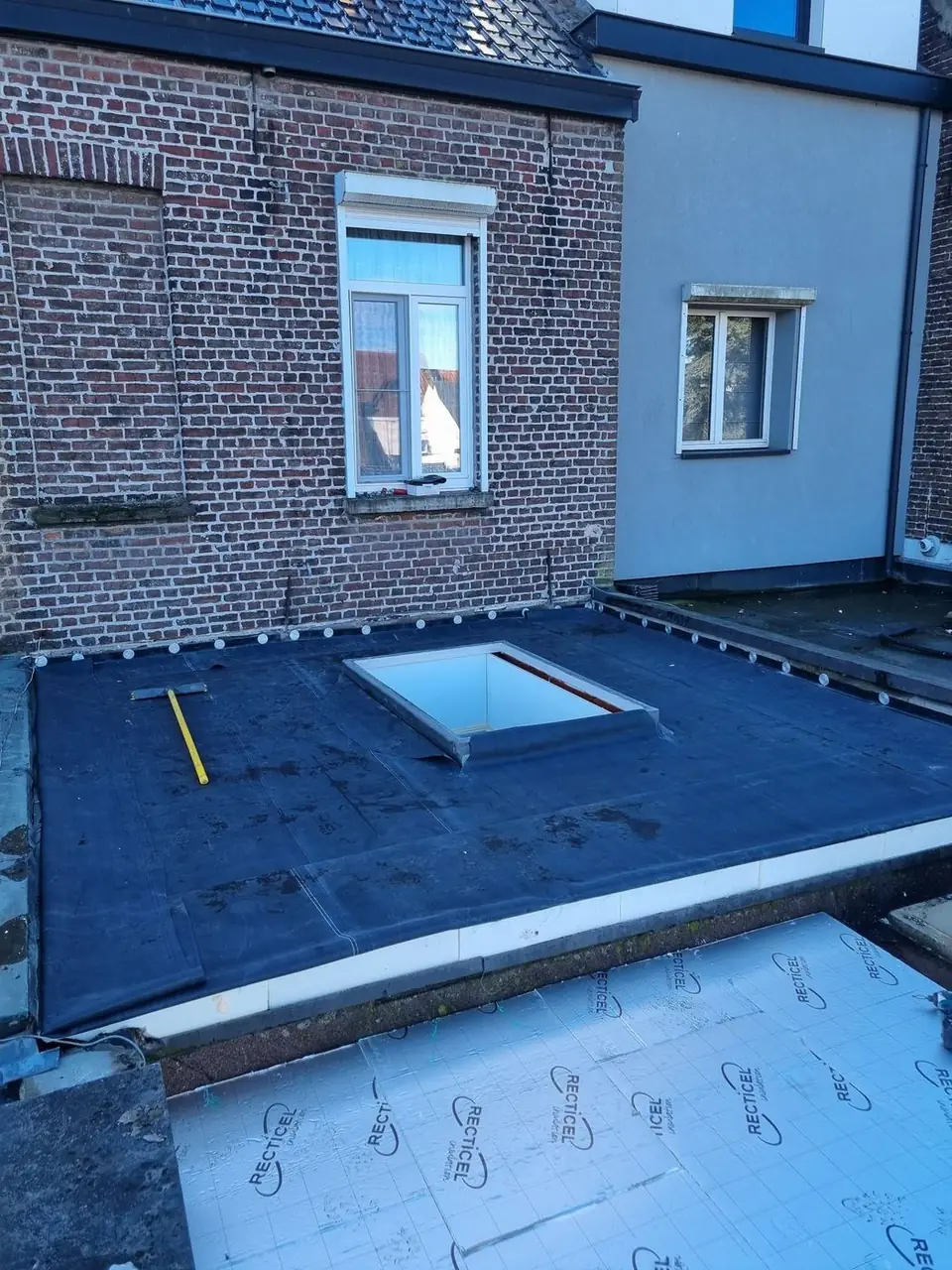 Plat dak met lichtkoepel naast een nieuw geïsoleerd dakvlak
