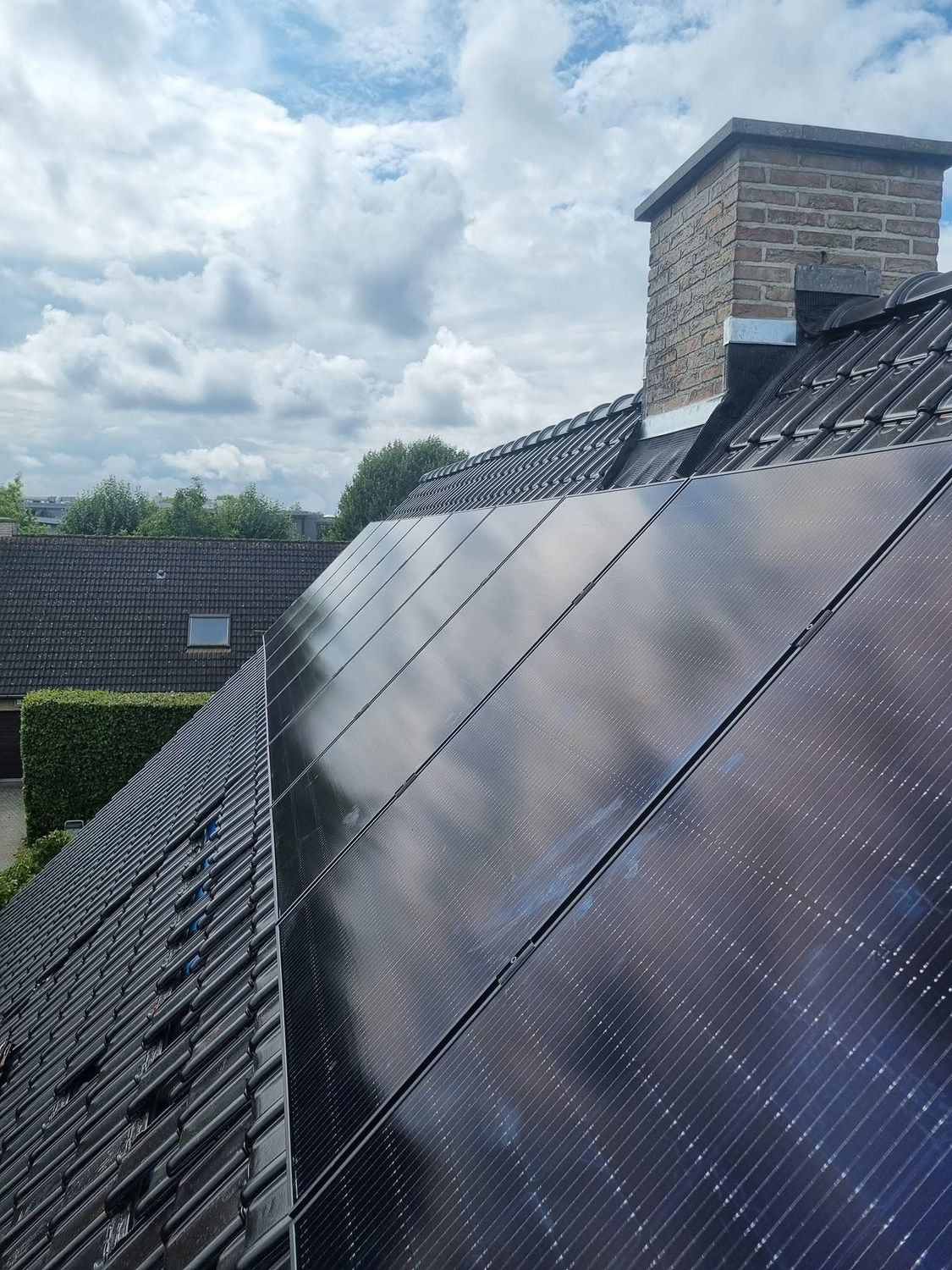 Zwarte zonnepanelen op een pannendak naast de schouw